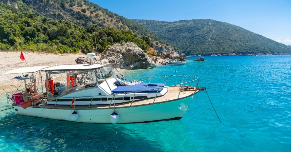 Passeio de barco em águas cristalinas em Prado, Bahia Barco ancorado em mar azul-turquesa próximo a praia cercada por morros verdes em Prado, Bahia
